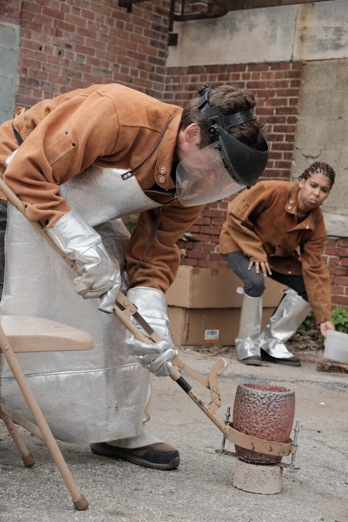 Chris Kane and Chanel (Nel) McNamara of Hot Funk Foundry at a metal pour event, wearing protective gear and handling equipment.