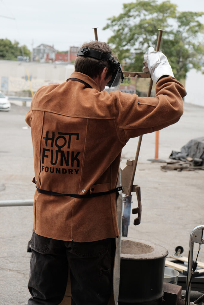 Founder and instructor Chris Kane at a metal pour event, wearing a "Hot Funk Foundry" jacket and protective gear.