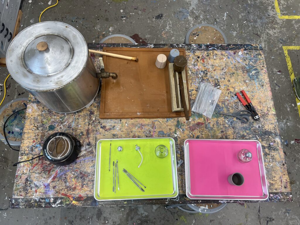 Tools and materials for a "Hot Funk Foundry" belt buckle workshop are arranged on a paint-splattered table.