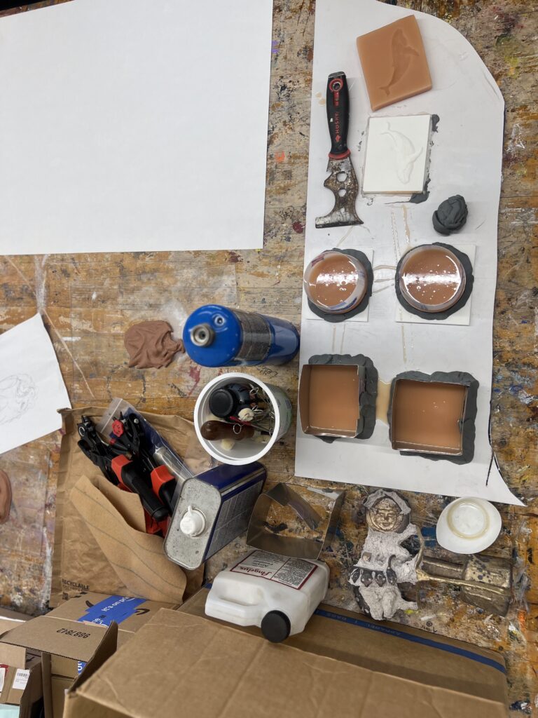 Tools and supplies for a belt buckle workshop, including molds, a torch, and various containers, arranged on a workbench.