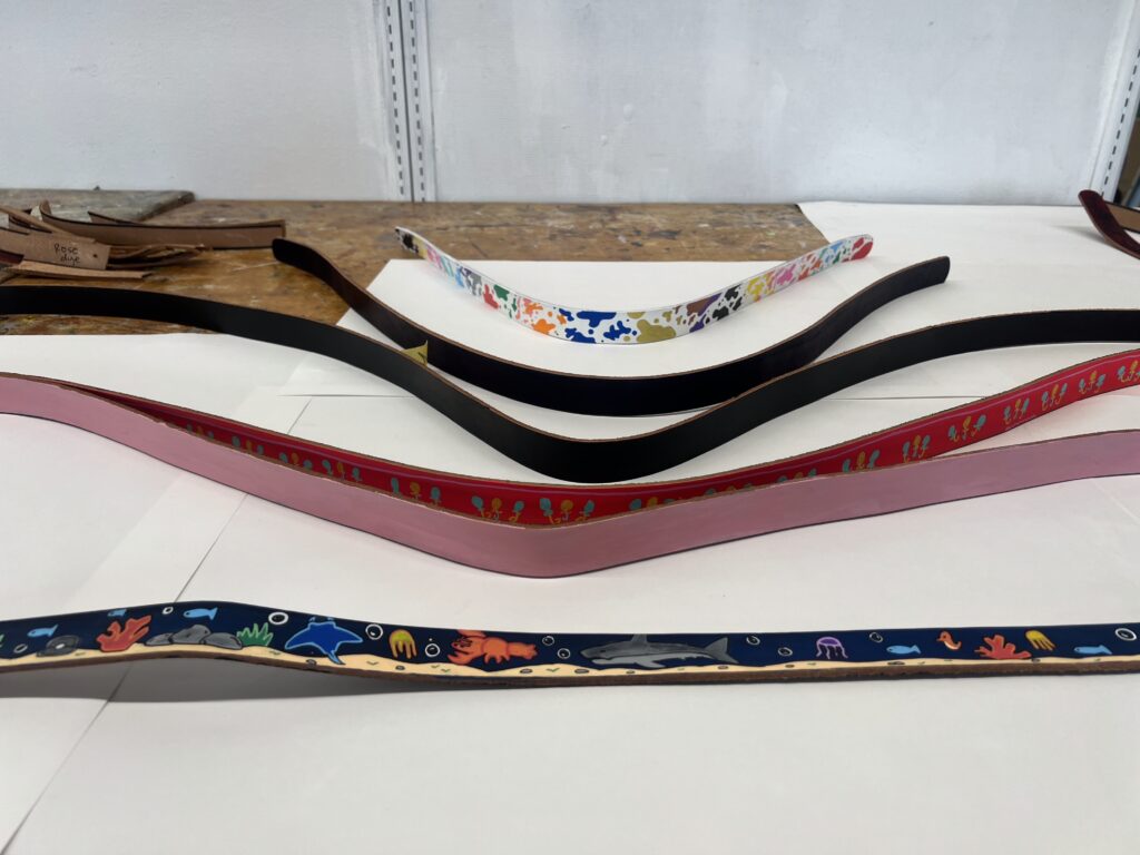 Colorful leather belt straps are laid out on a table, each featuring unique patterns and designs.