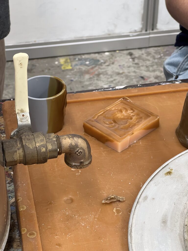 A workshop table with a mold for a bronze belt buckle, a metal spout, and a knife. Part of Chris Kane's workshop.