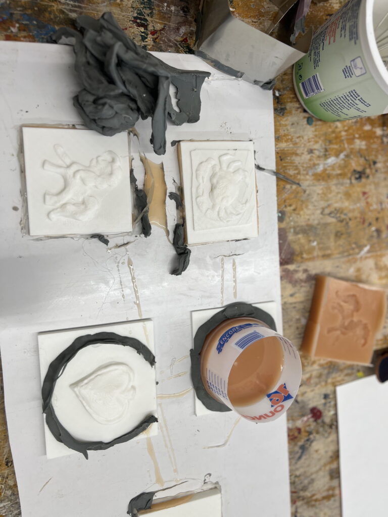 Clay molds and designs on a workbench, including a heart and abstract shapes, with tools and materials scattered around.
